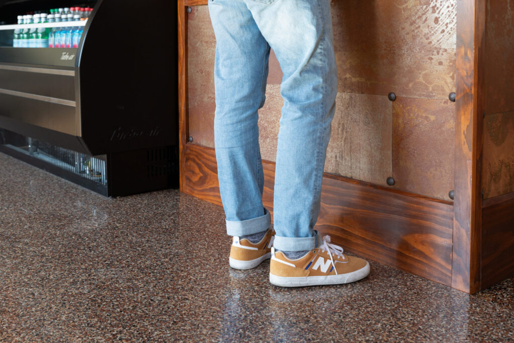 A shot of a high-gloss, decorative flake floor coating in a commercial retail setting. The textured surface features a dense, warm blend of brown, tan, and black flakes with a highly reflective finish.